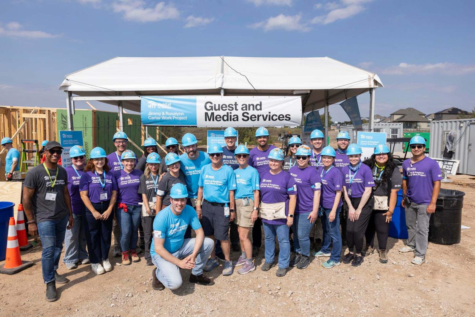 Habitat media volunteers stand in a group in front of the media tent at Carter Work Project in Austin, Texas.