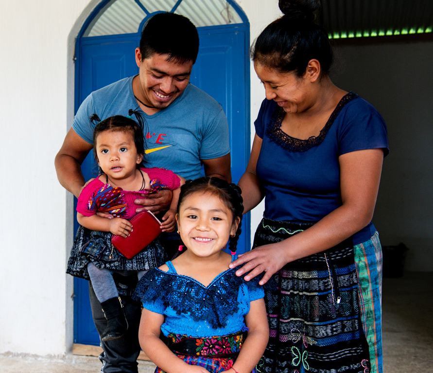 A family of four stands in front of a bright blue door and smiles for the camera.