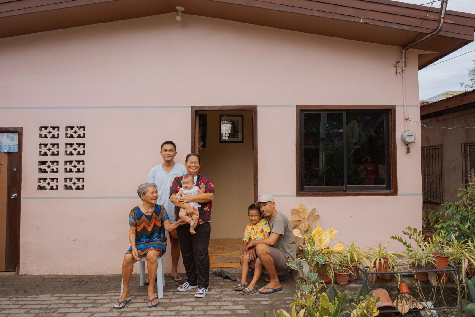 A family of five sits on either side of the front door to their peach-colored home and smile for the camera.