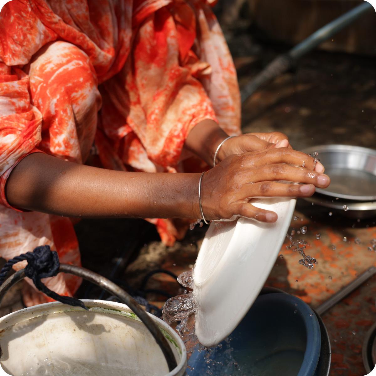 Close-up photo of hands washing a dish at a community well.