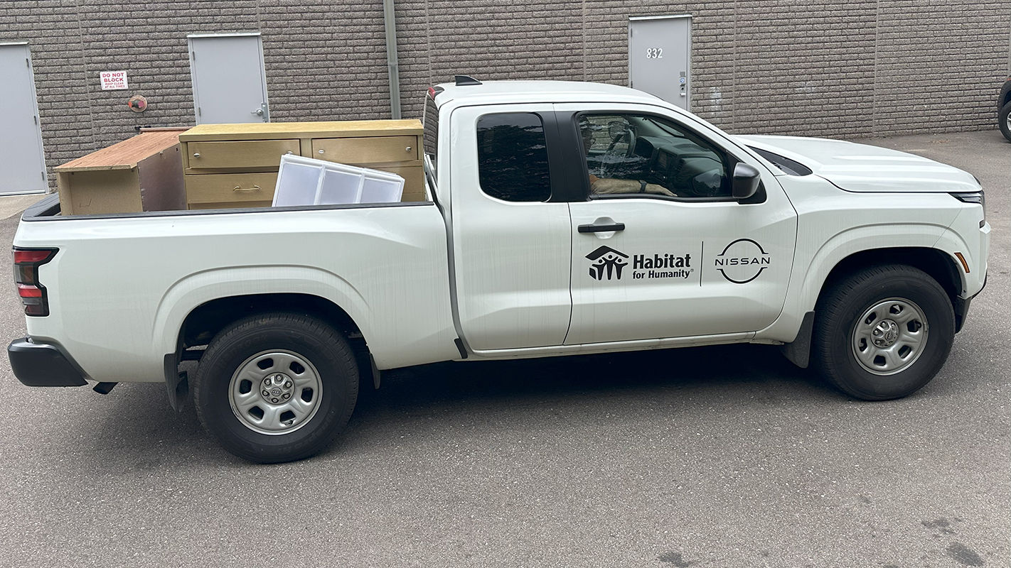 White pickup truck with Habitat for Humanity and Nissan logos on the side. The bed of the truck is full of furniture donations..