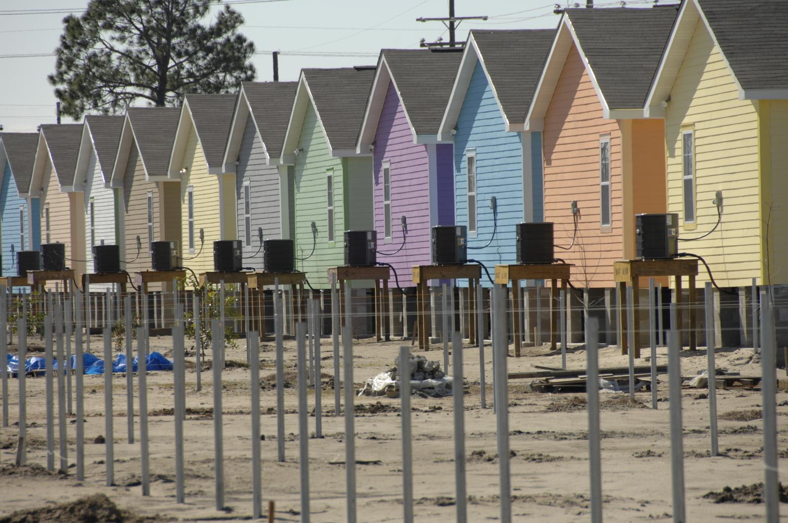 Row of rear exteriors of complete and near complete Habitat houses in Musician's Village with fence poles in the foreground.