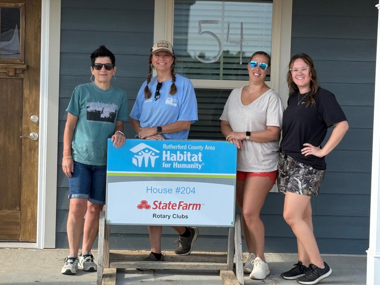 Four State Farm employees posing on a porch with a Habitat and State Farm partnership sign.