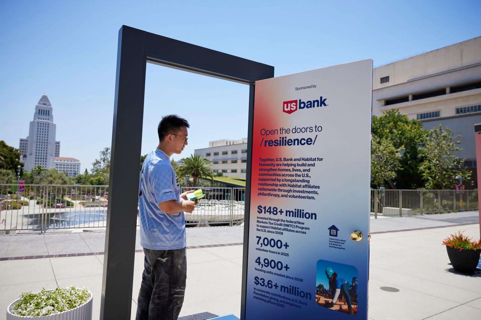 A man in a tie-dye shirt and jeans wearing a door sponsored by U.S. Bank. 