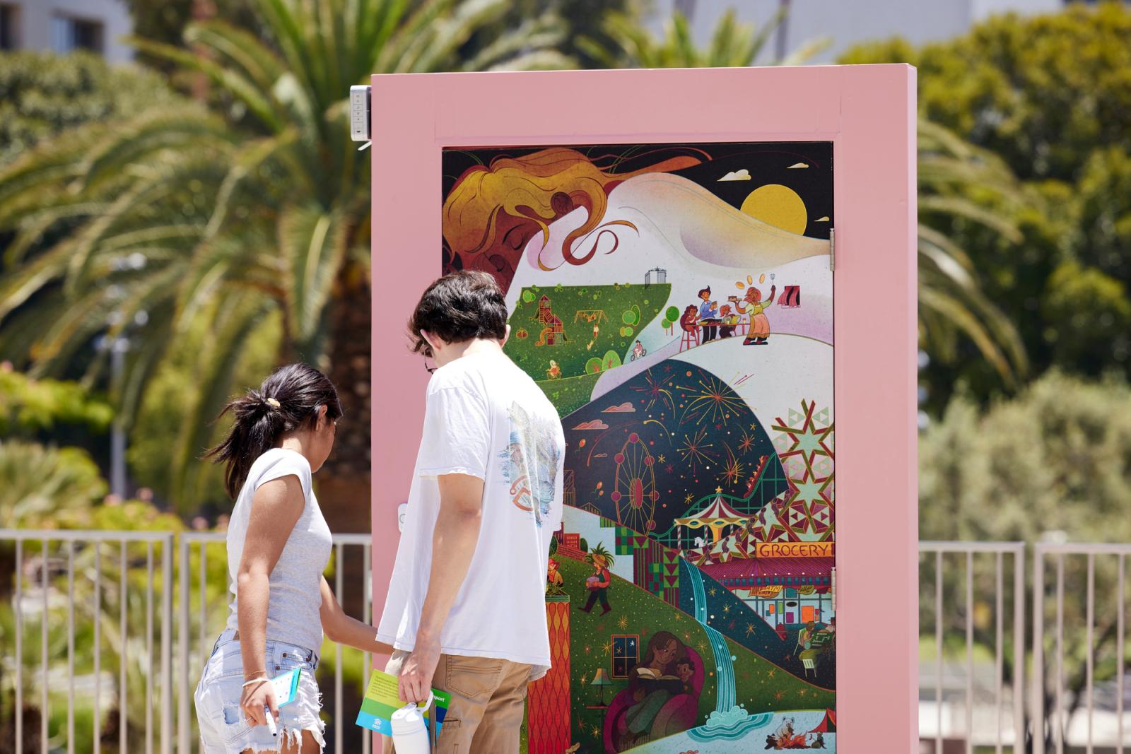 A woman and man viewing an illustrated door with a pink door frame.