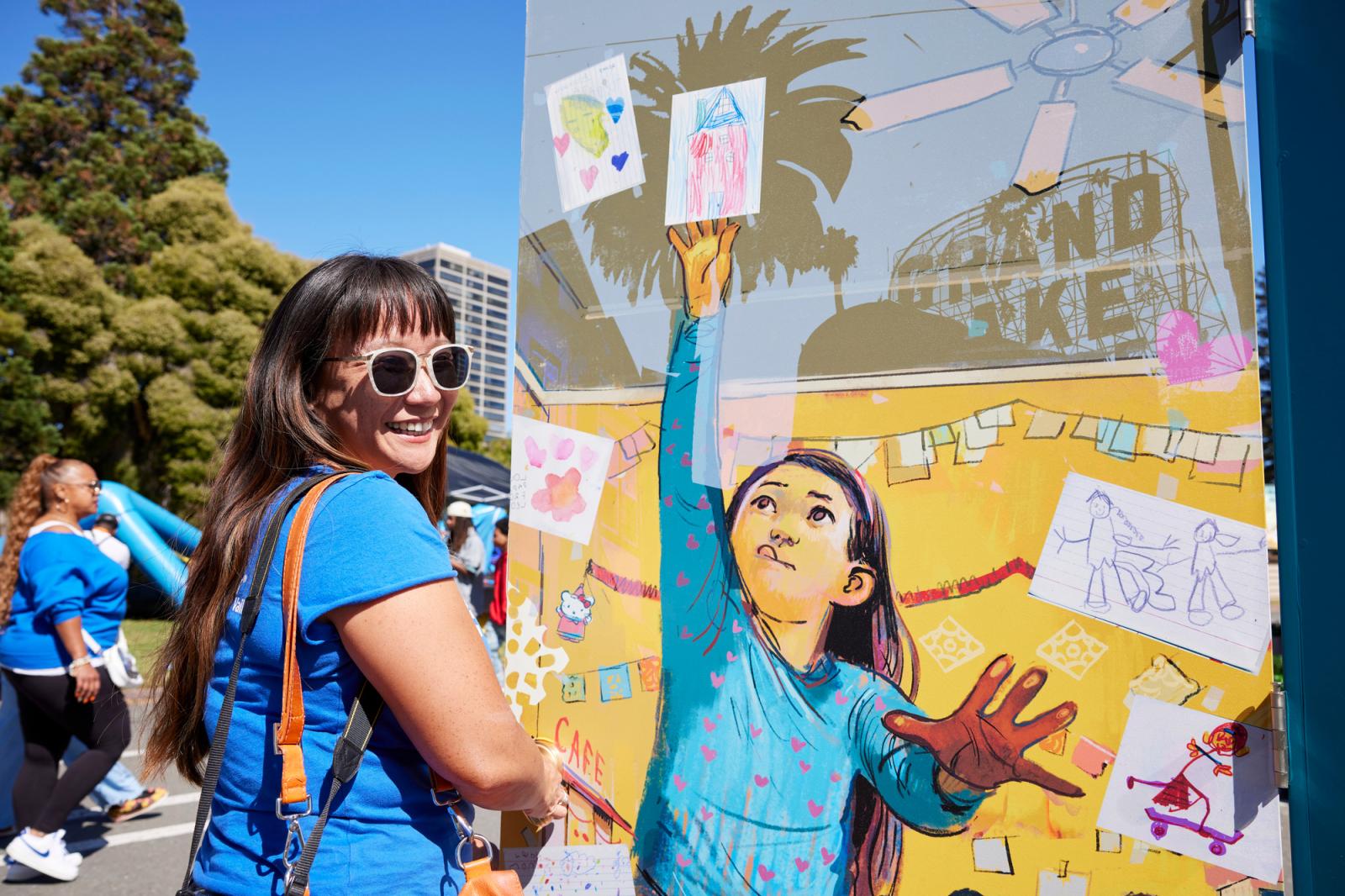 Woman in a blue shirt and sunglasses posing in front of an illustrated door with a little girl on it.
