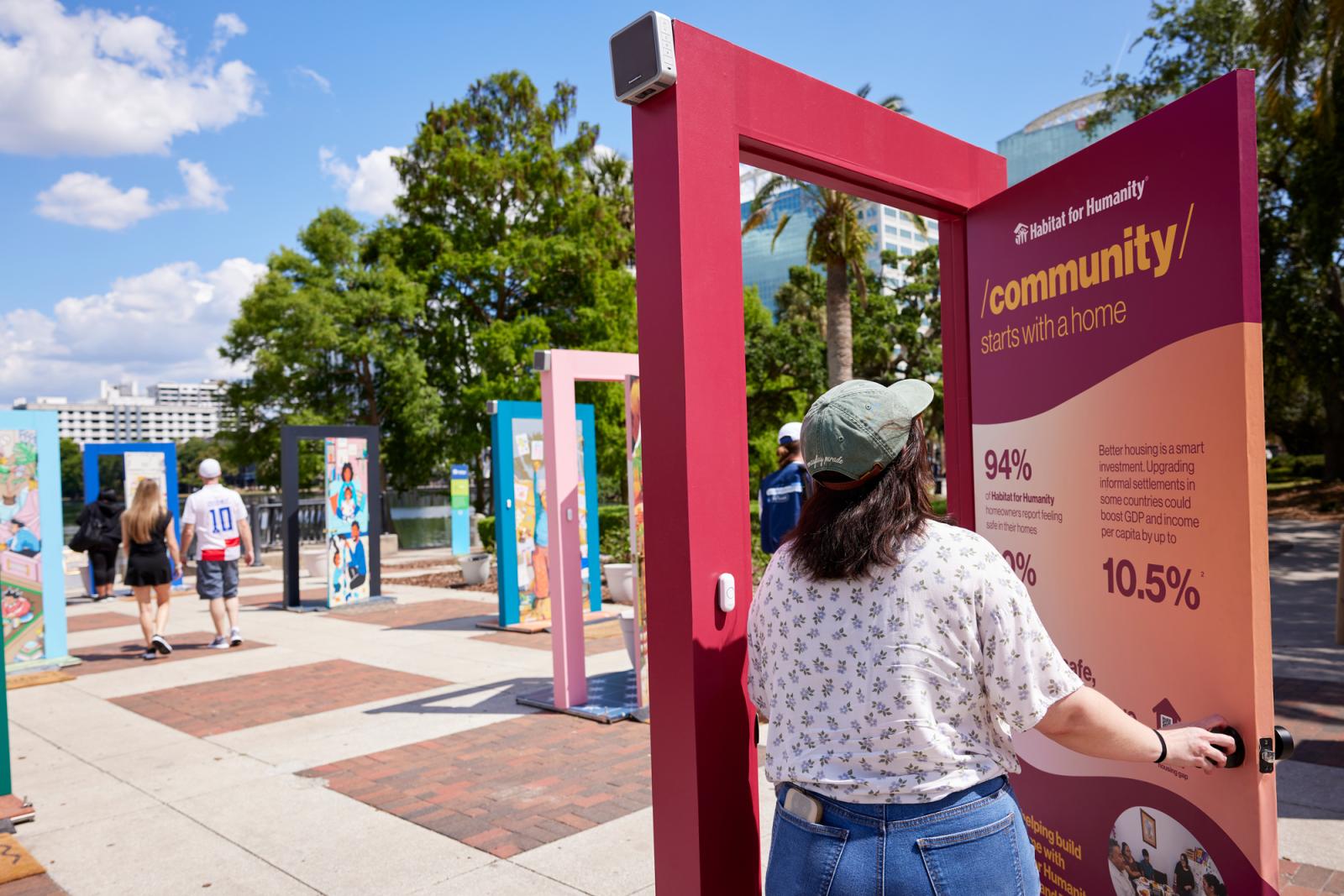 Woman in a white patterned shirt, jeans, hat and brown hair viewing a red door that displays the impact of home on sustainability.