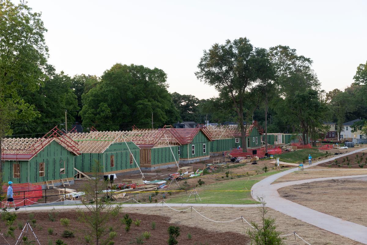 View of a park space with path branching off toward a row of partially-completed homes clad in green insulation.