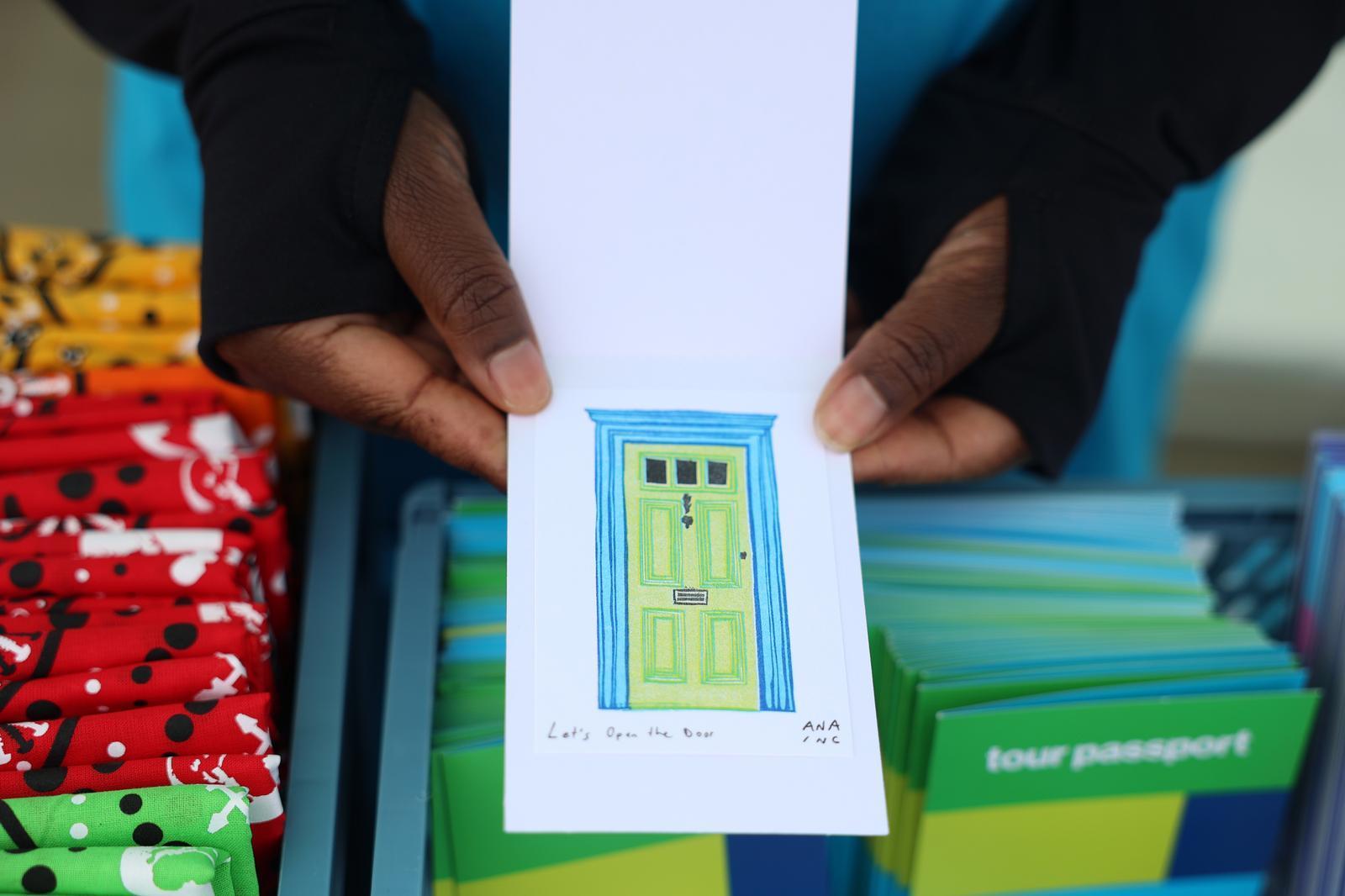Two hands holding a mini print of a green door with a blue frame.