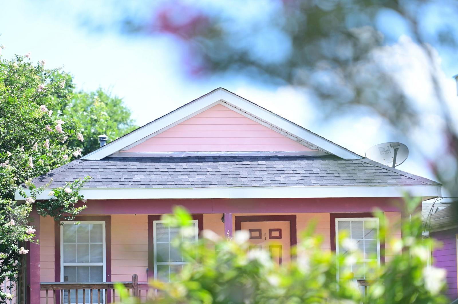 Pink house with gray roof and three windows on the front side of the house.