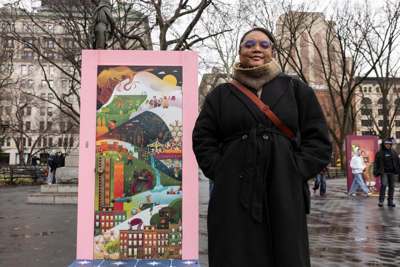 Woman in a long black coat standing in front of a door covered in an illustration with a pink frame.