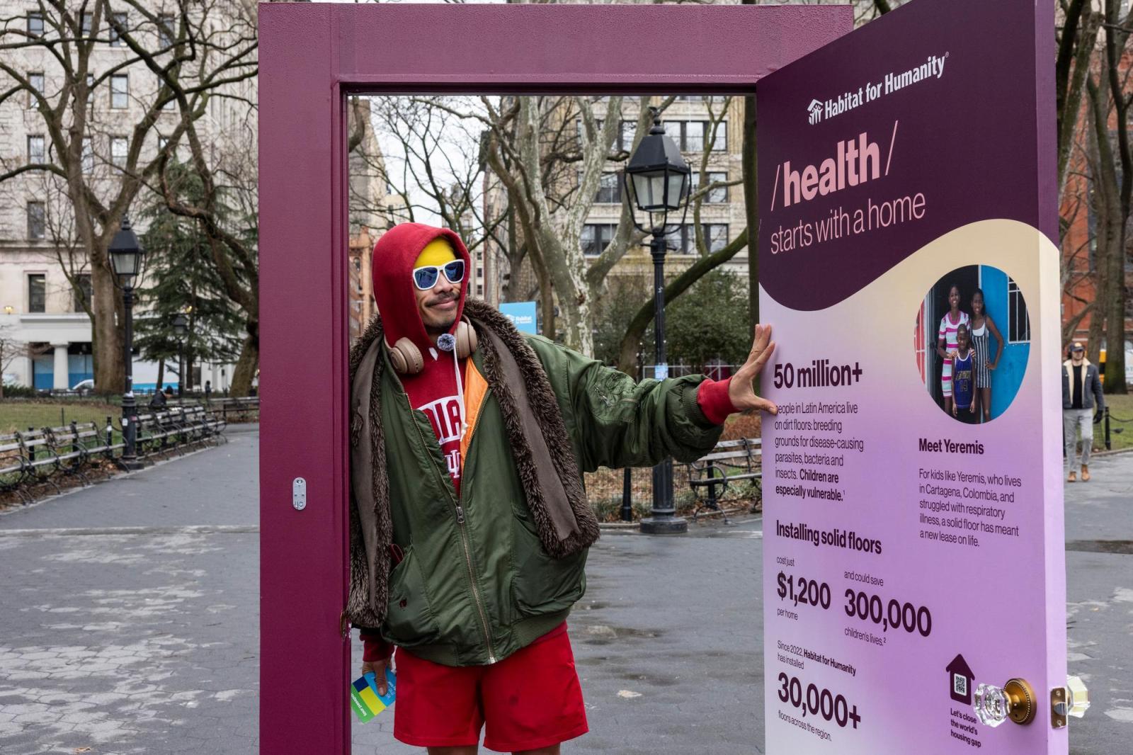Man in red shorts and a red hoodie with a green raincoat on and headphones are his neck leaning on the door frame of a purple illustrated door talking about how home affect health outcomes.