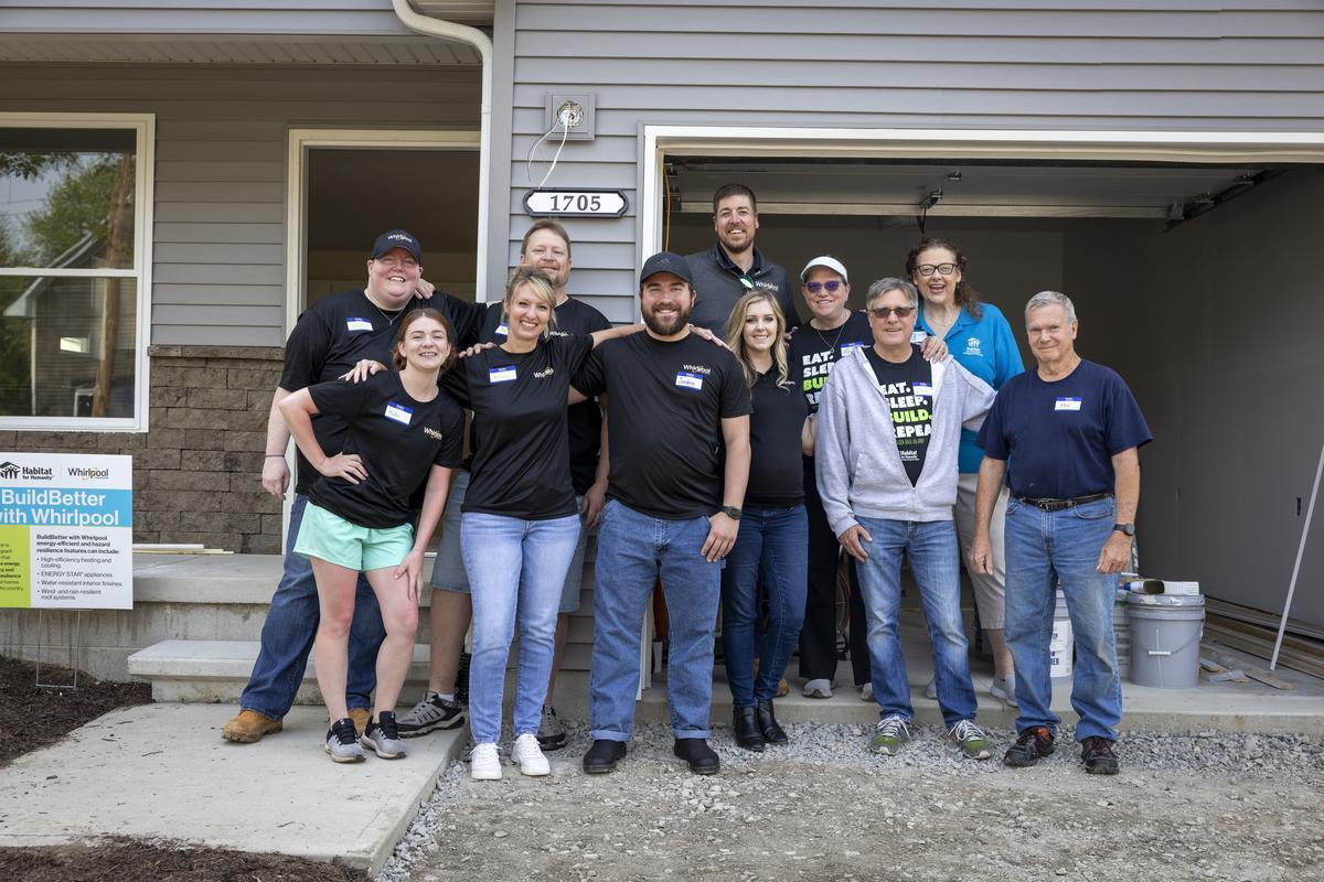 A group of Whirlpool employee volunteers pose in front of a house.