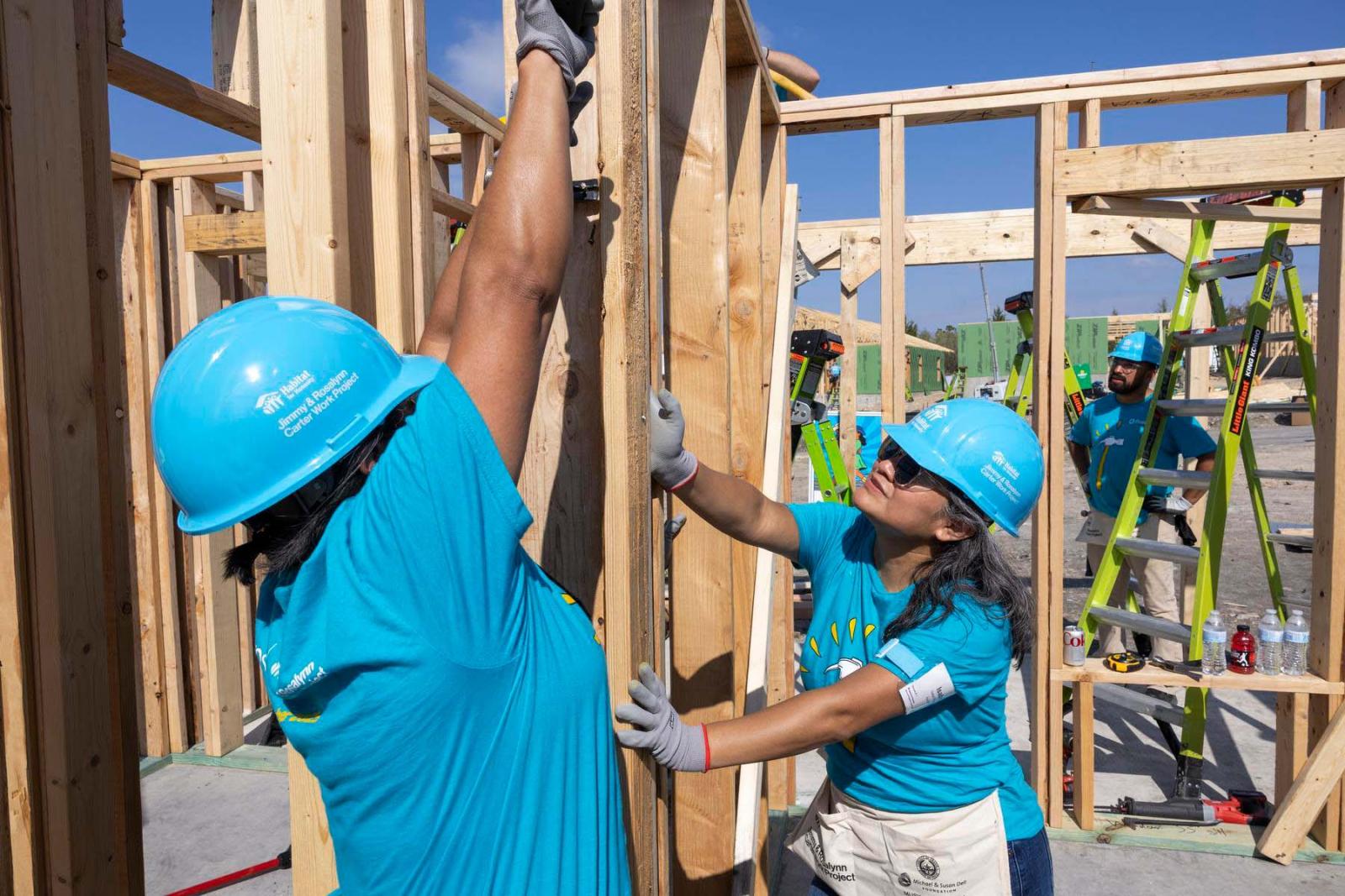 Two volunteers stand with their arms up holding pieces of lumber in place.