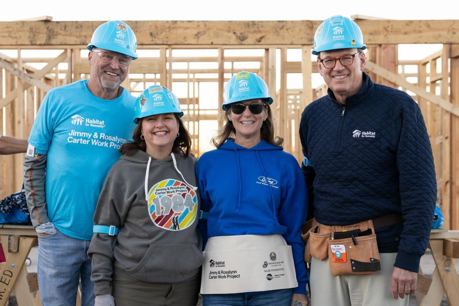 A group stands with blue Habitat hard hats on wearing both Habitat and Ford shirts.