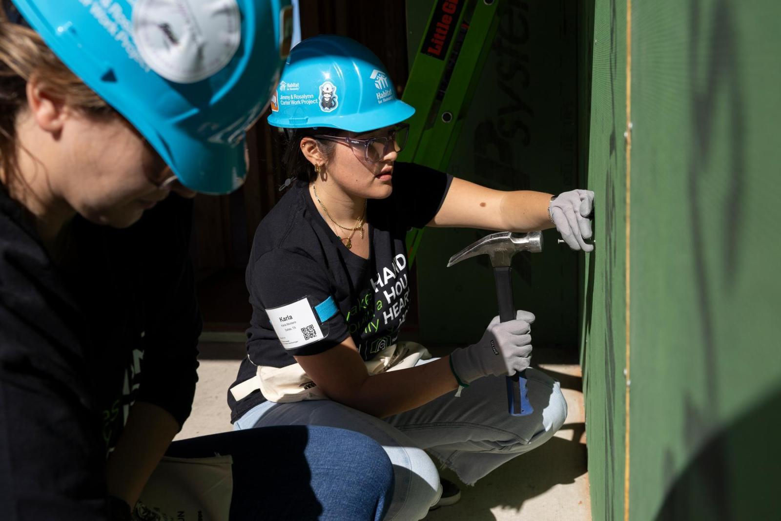 A volunteer in a black t-shirt squats down to work on the frame of a house.