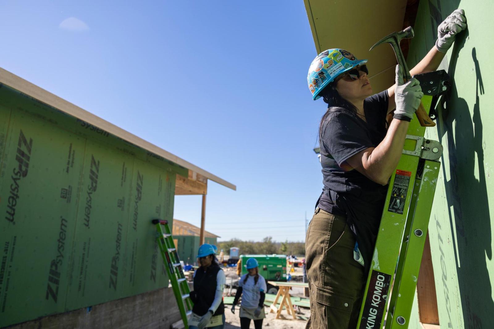 A volunteer stands on a ladder to work on the roofline of a build in progress.