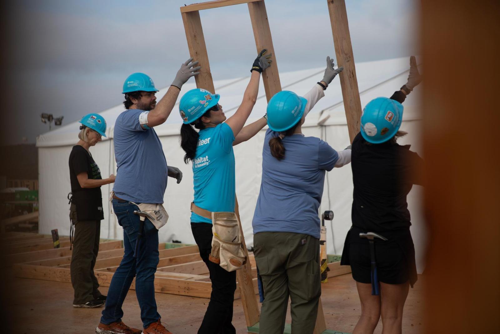 A team of volunteers lifts the frame of a house up in to place.