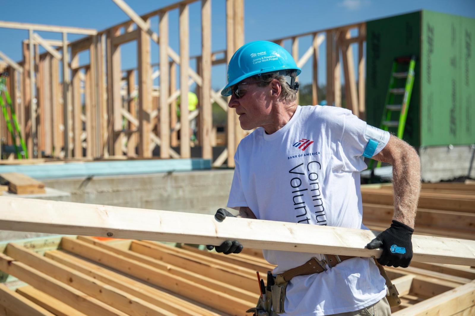 Bank of America employee in a hard hat caring lumber on a job site.