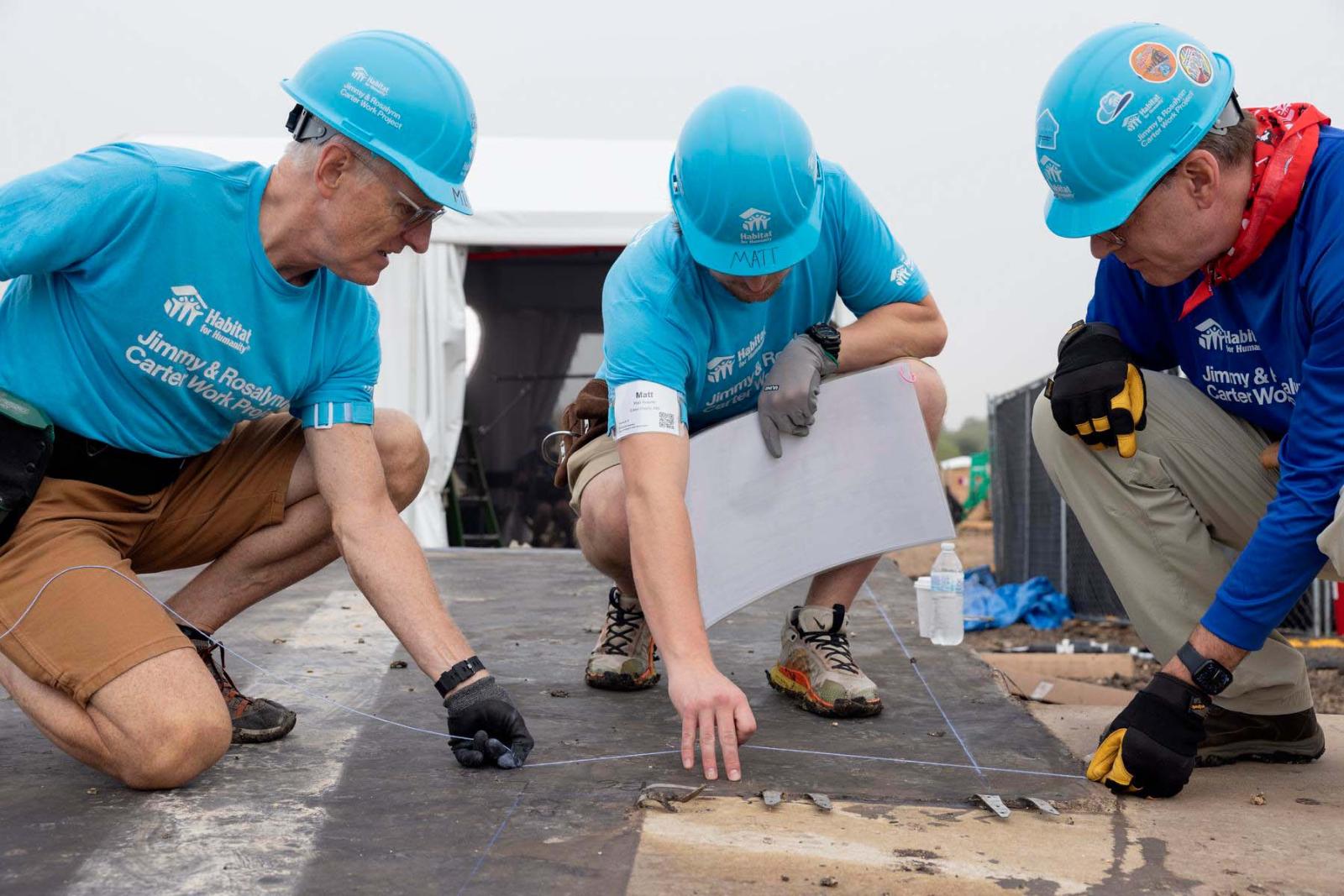Jonathan Reckford, CEO, Habitat for Humanity International, squats down with Matt Koepke and another volunteer to inspect the foundation of build site.