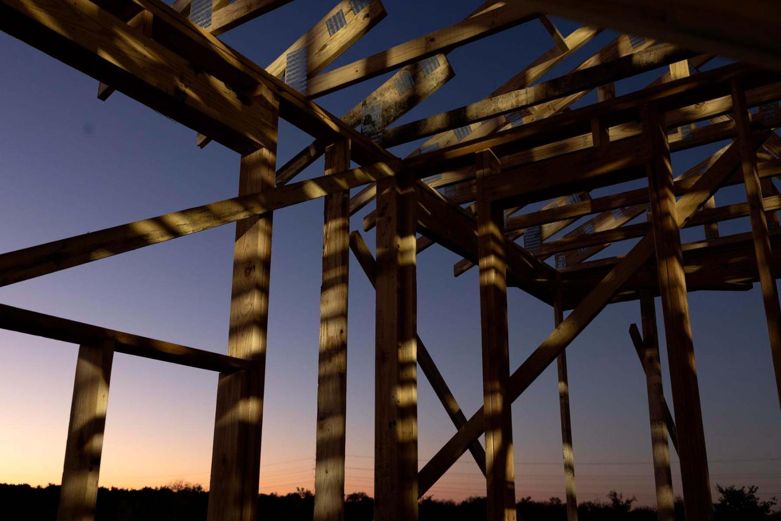 Wooden frame of a house build backlit against the sky as the sun rises.