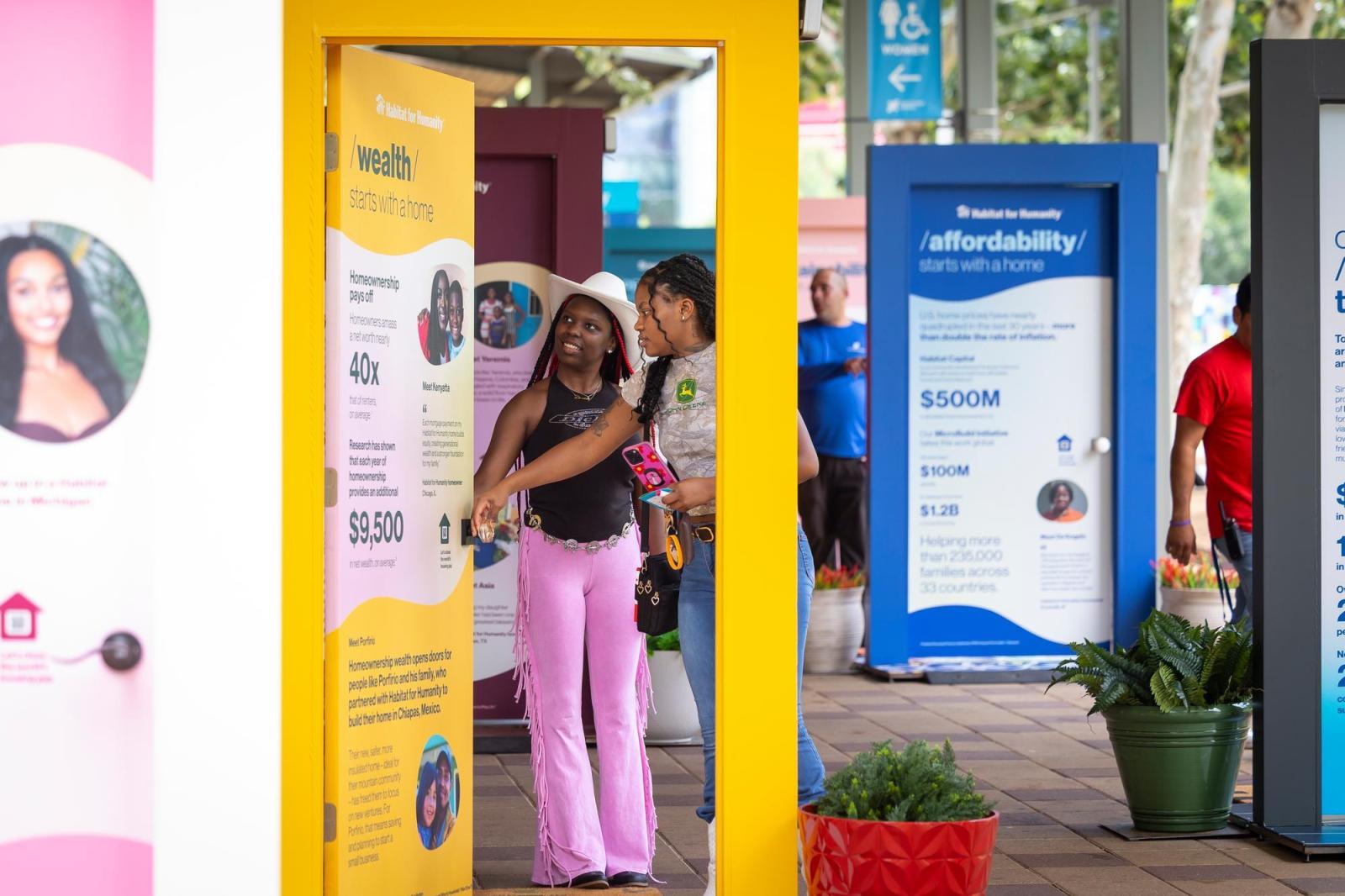 Girl in pink fringe pants and a black top viewing a yellow door with her friend.