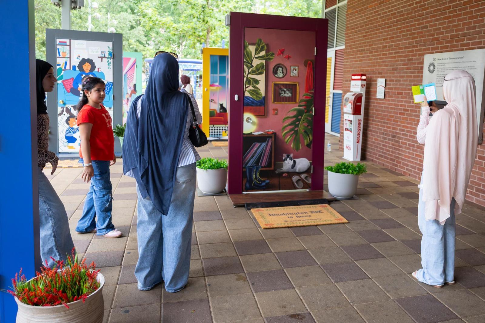 Two women in hijabs and a young boy viewing an illustrated door.