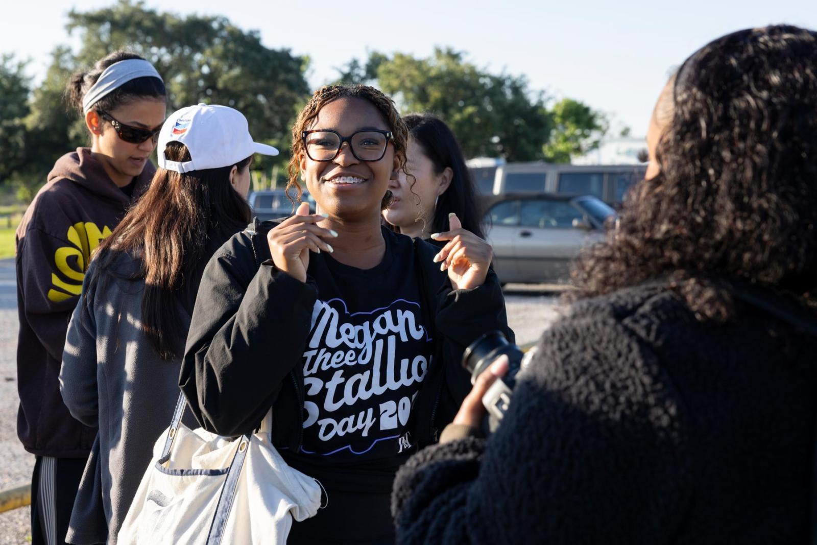 A volunteer holding a bag and wearing a black t-shirts smiles at the camera and holds up her hand in greeting.