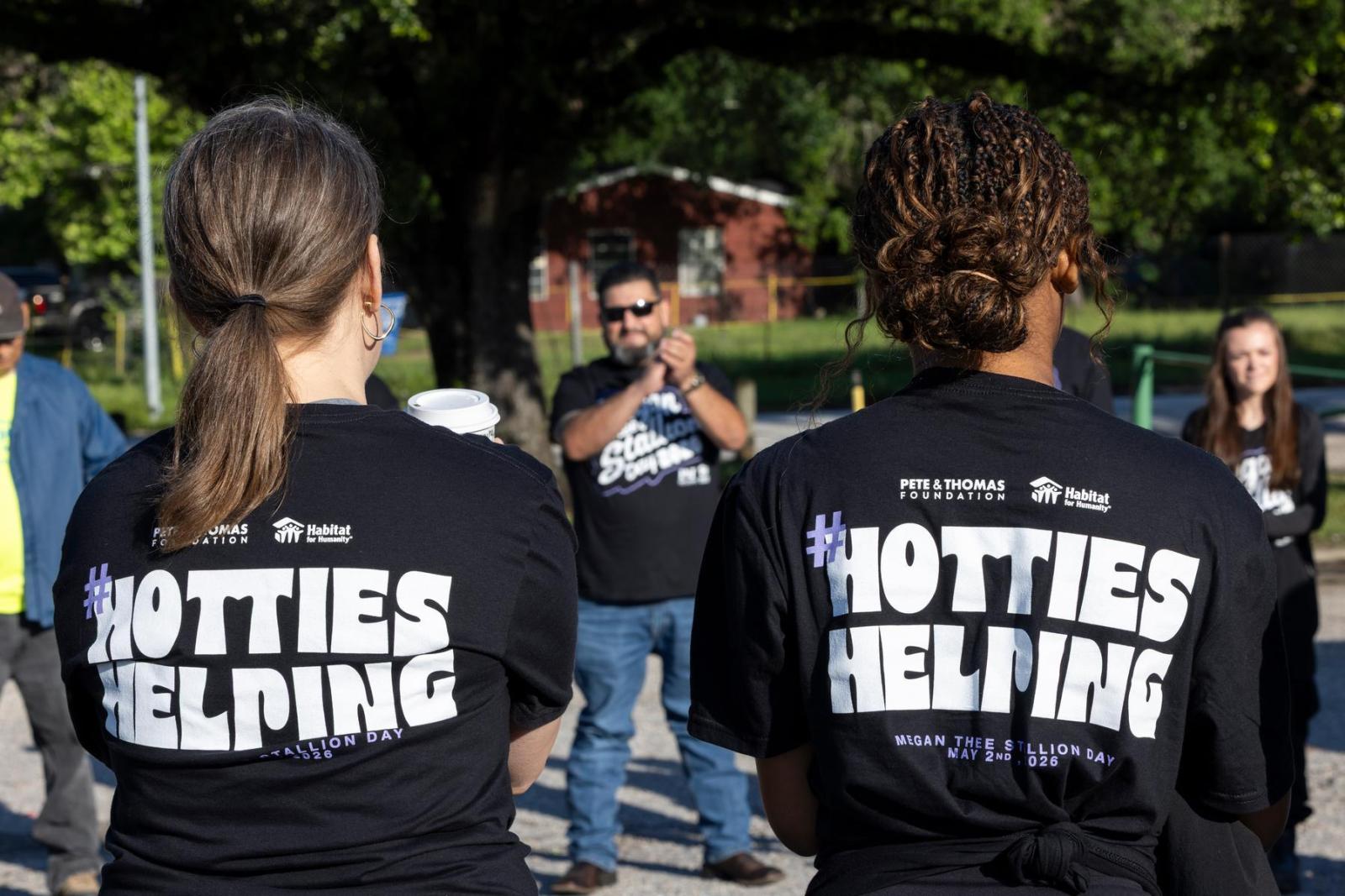 Two volunteers in Hotties Helping t-shirts stand in a circle with other volunteers as they receive instructions.