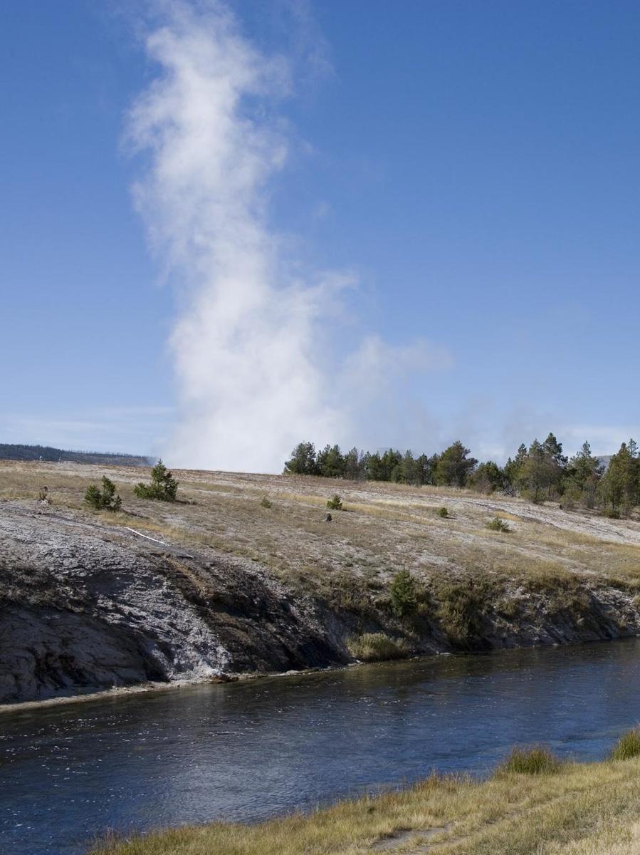 A landscape view of Yellowstone National Park featuring water and green land with steam rising above it to illustrate geothermal energy.