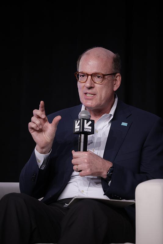 CEO Jonathan Reckford sitting on the South by Southwest panel and stage holding a microphone.
