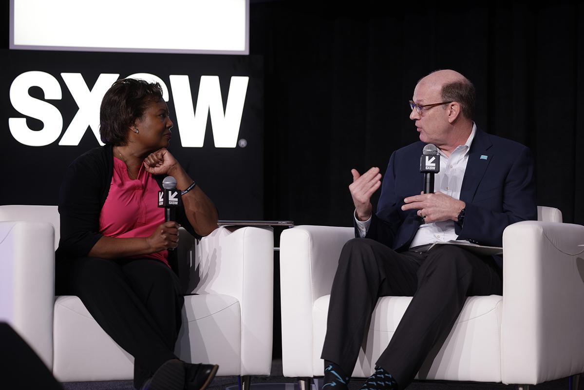 Habitat CEO Jonathan Reckford and another panelist sitting in white chairs on stage at South by Southwest in mid-conversation.