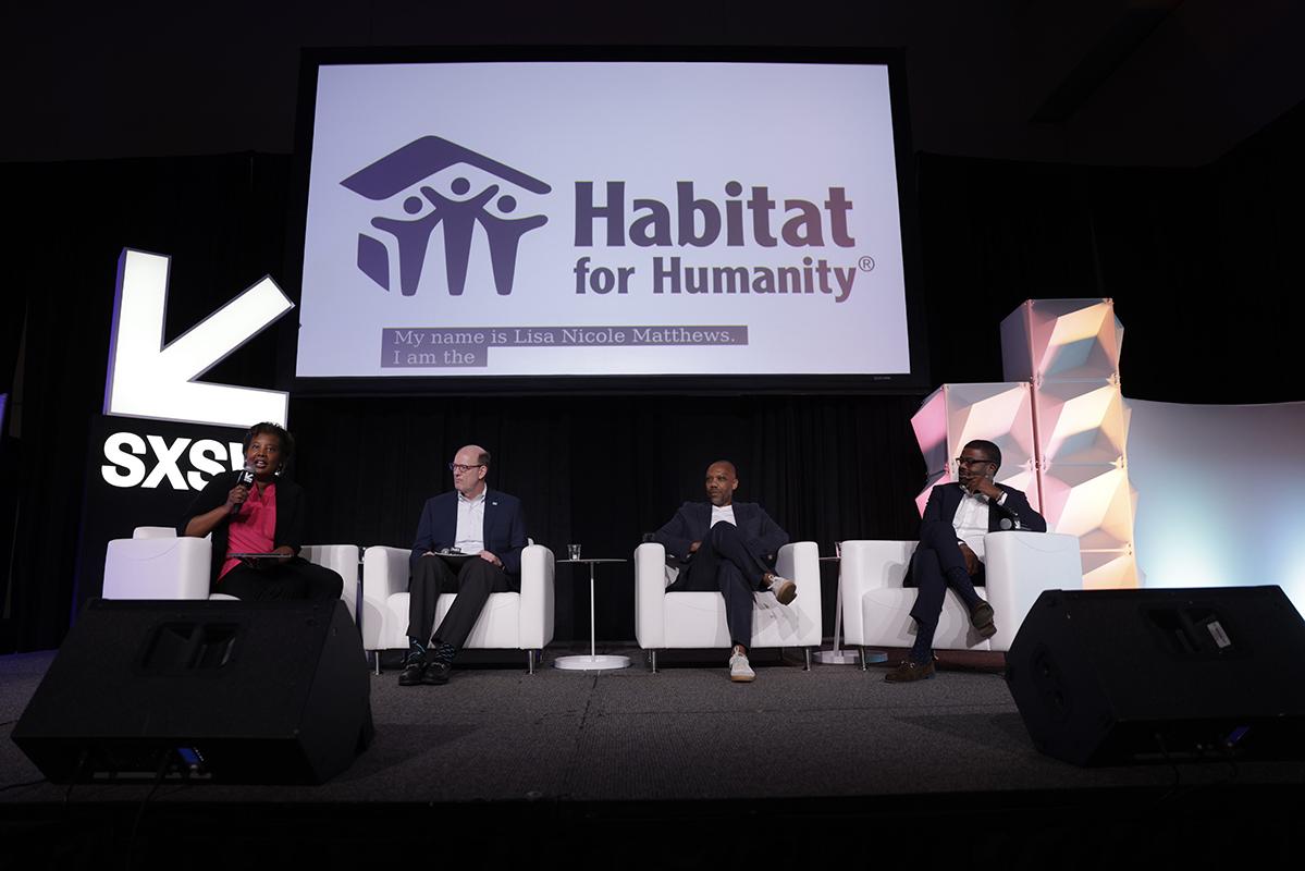 Four people including Habitat CEO Jonathan Reckford sitting on a stage for a panel discussion at South by Southwest with a white Habitat banner above their heads.