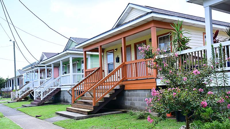 A row of colorful cottages with wide, welcoming front porches line a sidewalk in New Orleans.