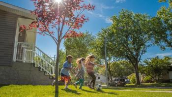 Three children playing soccer in front yard of Habitat home.