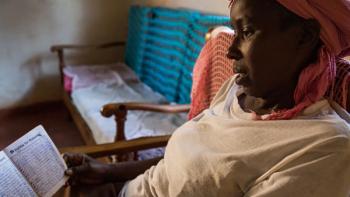 a woman from Kenya sitting on a chair holding an open book with her microloan payments