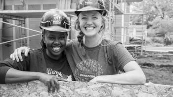 Two smiling volunteers in hard hats on a Habitat build site.