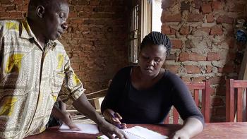 a woman from Uganda sitting at the table. She is studying her microloan payments book.