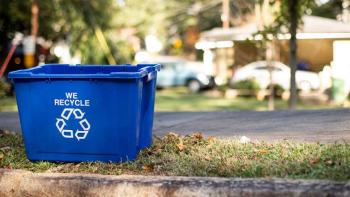 blue recycling bin on curb with cars in the background.