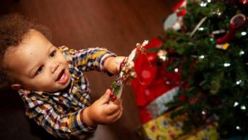 Little boy hangs ornament on Christmas tree. 
