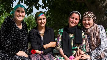 Photo: four women holding roses sitting on a bench under the tree