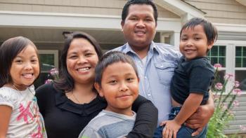 family of five smiling in front of house. 