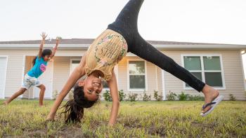 Two girls cartwheeling in front of home. 