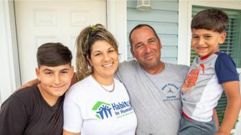 Parents with two sons smiling in front of house. 