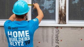 Volunteer wearing a shirt that says "Home Builders Blitz 2019" works on a window on a build site.