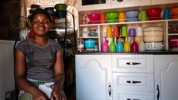 Photo: Lucy in her kitchen. Colorful dishes tidied up in the cupboard behind her.