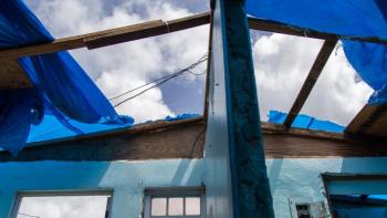 View from inside hurricane-damaged house of missing roof with blue tarps partially covering.