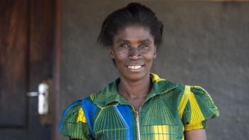 Habitat homeowner Joyce smiling in front of her home in bright green dress.