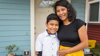 Woman and son standing and smiling in front of their Habitat home.