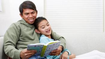 A little girl and her father reading on a couch together. 